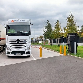 Zwei Lkw stehen neben einer Ladesäule für E-Lkw.