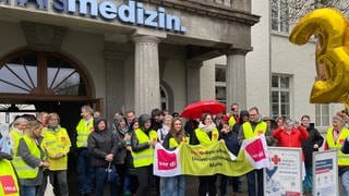 Nicht-ärztliches Personal der Mainzer Unimedizin steht mit Plakaten vor dem Eingang des Krankenhauses