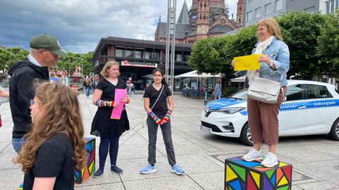 Eine Frau steht mit einem Zettel in der Hand auf einer Kiste: Das ist Teil einer Aktion von Schülern des Mainzer Gutenberg-Gymnasiums für Demokratie und Vielfalt