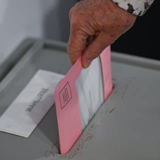 Die ausgefüllten Wahlunterlagen werden in eine Wahlurne geworfen. In Gensingen ist die Wahl zum Ortsbürgermeister jetzt aber verschoben worden.