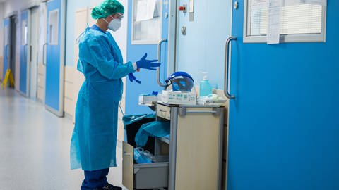 Eine Krankenhausmitarbeiterin in Corona-Schutzkleidung steht alleine in einem Krankenhausflur.