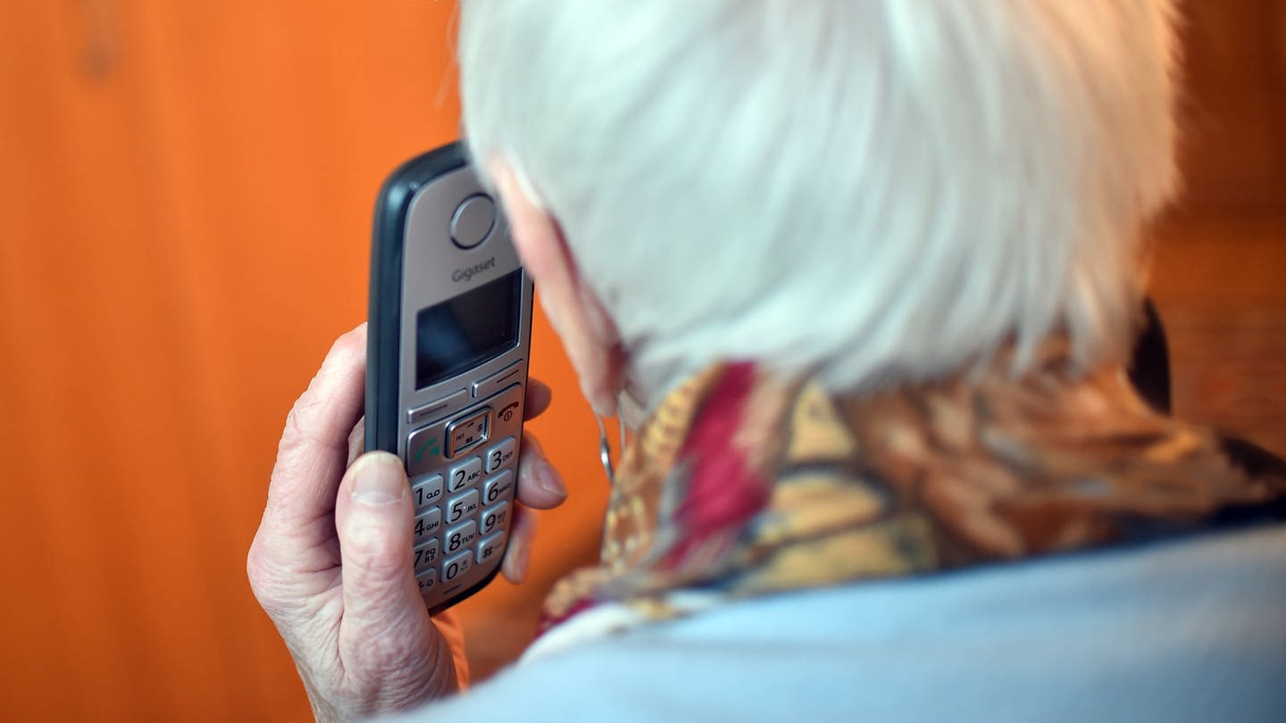Eine Seniorin hält ein Telefon in der Hand.