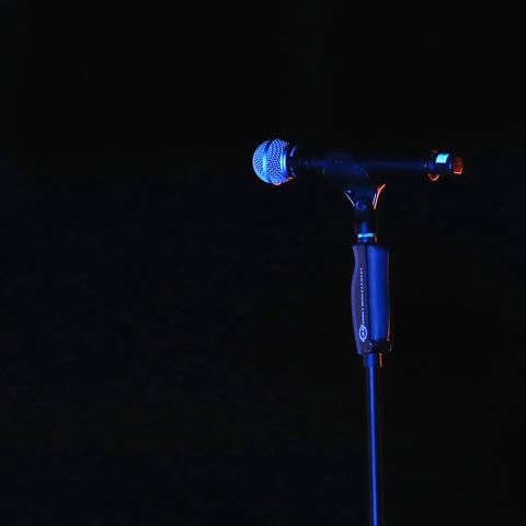 Ein Mikrofon steht alleine in einer dunklen Halle auf einem Mikrofonständer.