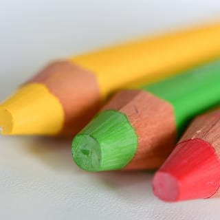 Drei Farbstifte in den Farben Rot, Grün und Gelb liegen nebeneinander auf einem Tisch (Foto: dpaArne Dedert)