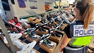 Eine spanische Polizistin steht vor einem Verkaufsstand mit gefälschten Markensportschuhen. 