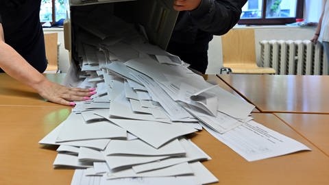 Wahlhelfer schütten eine Wahlurne mit Stimmzetteln aus.