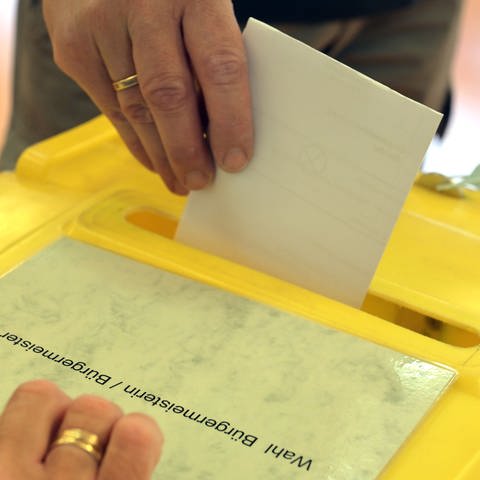 Ein Wähler wirft steckt einen Wahlzettel in eine Wahlurne. 