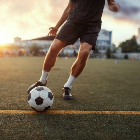 Ein junger Mann schießt auf einem Fußballplatz gegen einen Ball. 