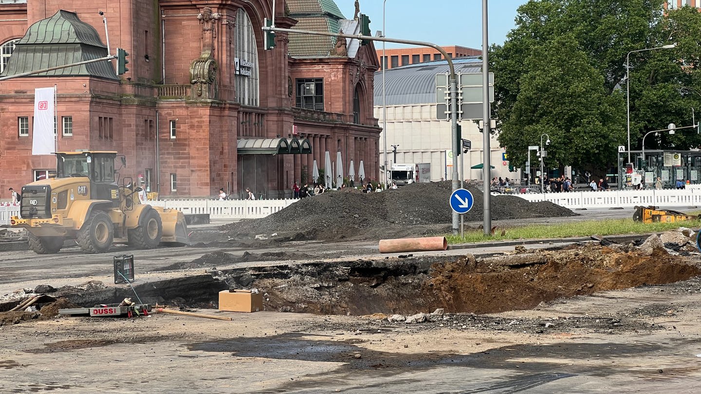 Im Straßenbelag ist ein Loch. Im Hintergrund sieht man die rote Fassade des Wiesbadener Hauptbahnhofs.