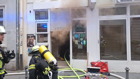 Rauch dringt aus einem Lokal in der Mainzer Altstadt, Feuerwehrleute löschen.