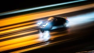 Ein Porsche rast nachts über eine regennasse Straße (Symbolbild).