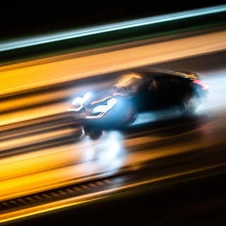 Ein Porsche rast nachts über eine regennasse Straße (Symbolbild).
