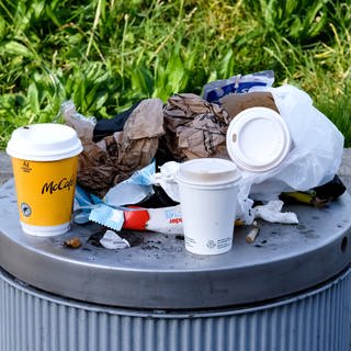 Auf einem vollen Mülleimer stehen leere Einweg-Kaffeebcher (Symbolbild).