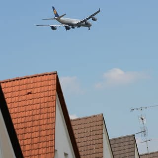 Ein Flugzeug überfliegt Häuser (Symbolbild). Durch ein neues Anflugverfahren soll Mainz vom Fluglärm entlastet werden. 