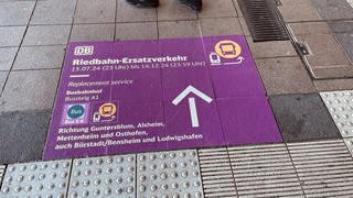 Hinweise auf dem Boden leiten die Fahrgäste am Wormser Hauptbahnhof zum Riedbahn-Ersatzverkehr. (SWR)