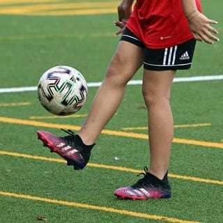 Ein Mädchen jongliert einen Ball auf einem Fußballplatz.