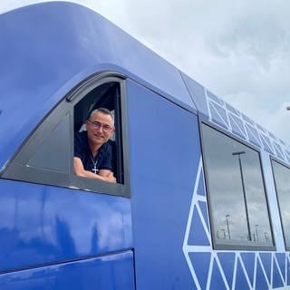 Lokführer Andreas Frank schaut aus dem Fenster seiner Fahrerkabine und lächelt  