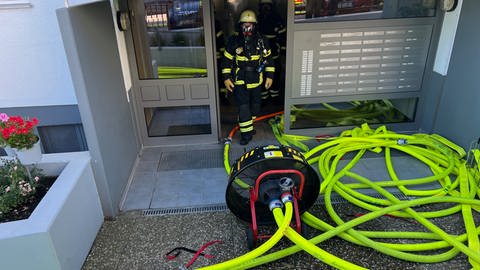 Einsatzkräfte der Feuerwehr Bad Kreuznach haben zum Löschen eines Feuers im Keller eines Mehrfamilienhauses zahlreiche gelbe Schläuche durch die Eingangstür verlegt.