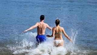 Ein Mann und eine Frau laufen in das kühle Wasser des Rheins. Vielerorts suchen die Menschen nach Abkühlung.