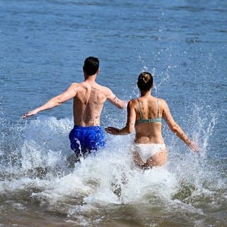 Ein Mann und eine Frau laufen in das kühle Wasser des Rheins. Vielerorts suchen die Menschen nach Abkühlung.