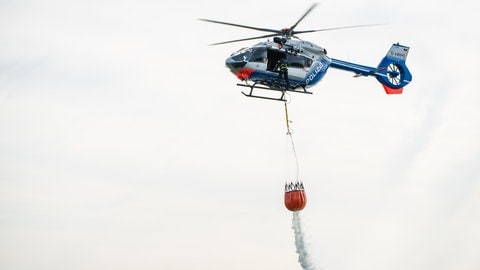 Ein fliegender Polizeihubschrauber lässt aus einem Sack Löschwasser ab.