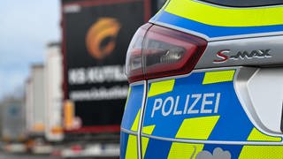 Das Heck eines Polizeiautos im Vordergrund, im Hintergrund unscharf eine Reihe Lkw.