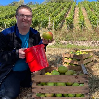 Daniel von den Lebenshilfe Werkstätten Bad Kreuznach freut sich sehr über die Äpfel, die Winzerin Ute Schweinhardt der Gruppe nach dem Apfelklau geschenkt hat.