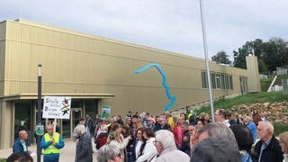 Vor der Rheinhessenhalle in Monsheim stehen Menschen und halten Protest-Schilder hoch.