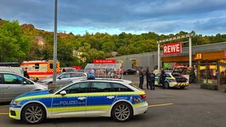 Polizei steht vor einem Supermarkt in Kirn, nachdem ein Mann einen anderen mit einem Messer im Gesicht verletzt hat.