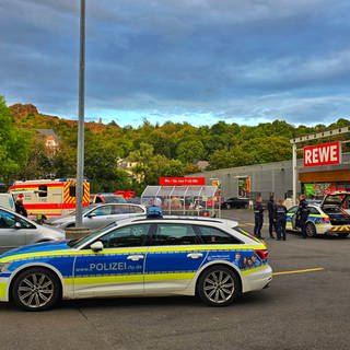 Polizei steht vor einem Supermarkt in Kirn, nachdem ein Mann einen anderen mit einem Messer im Gesicht verletzt hat.