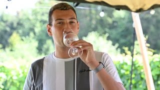 Levin McKenzie aus Wackernheim steht mit einem Gläschen Wein im Weinberg. Er ist der erste Weinkönig im Anbaugebiet Rheinhessen. 