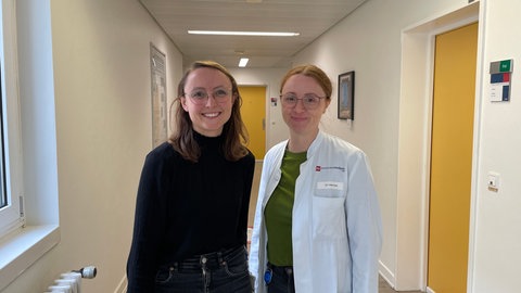 Alisa Düben und Isabel Heinrich von Gedächtnisambulanz der Universitätsmedizin Mainz stehen nebeneinander in einem Gang der Klinik.