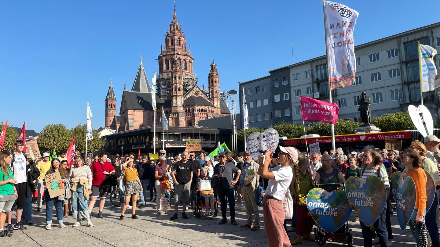 Klimastreik in Mainz: Eine Menschengruppe mit Plakaten steht am Theatervorplatz in Mainz und lauscht einer Frau, die ein Megaphone in der Hand hat.