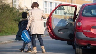 Eine Mutter lässt ihr Schulkind aus dem Auto aussteigen.