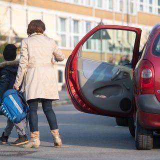 Eine Mutter lässt ihr Schulkind aus dem Auto aussteigen.