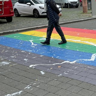 Menschen laufen über eine Zebrastreifen in den Farben des Regenbogens. In Mainz ist der Regenbogen-Zebrastreifen-mit-Farbe-beschmiert-worden