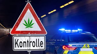 Ein Warnschild mit Cannabissymbol vor einem Polizeiauto. (Symbolbild) In Mainz hat die Polizei bei einer Kontrolle bei einem Autofahrer Haschisch in der Unterhose entdeckt. 