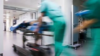 Eine Patientin auf einer Liege wird im Krankenhaus einen Flur entlang geschoben.