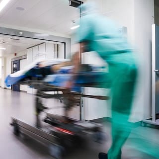 Eine Patientin auf einer Liege wird im Krankenhaus einen Flur entlang geschoben.