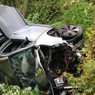 Ein völlig demoliertes Auto liegt auf der Seite im Gebüsch. Bei einem Unfall auf der Saarstraße in Mainz sind fünf Menschen verletzt worden. 