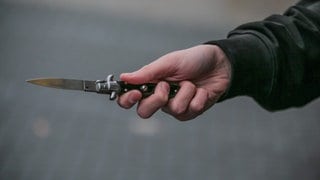 Eine Männerhand mit einem Messer in einer Hand. Bei einem Tankstellenüberfall in Mainz hat der Täter die Angestellte mit einem Messer bedroht. 