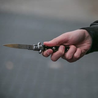 Eine Männerhand mit einem Messer in einer Hand. Bei einem Tankstellenüberfall in Mainz hat der Täter die Angestellte mit einem Messer bedroht. 