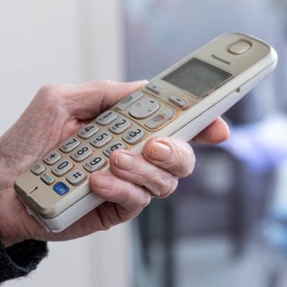 Eine ältere Frauenhand hält ein Telefon in der Hand. In Bad Kreuznach steht ein Mann vor Gericht, der seine Opfer mit Schockanrufen übers Ohr gehauen haben soll. 