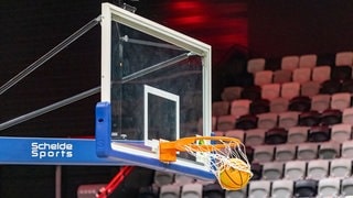 Ein Basketball landet vor einer Zuschauertribüne im Korb.