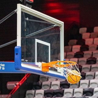 Ein Basketball landet vor einer Zuschauertribüne im Korb.