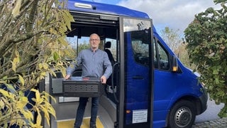 Busfahrer Ralf Werner trägt die Kiste mit einer Bestellung aus dem Ruf-Bus, um sie an eine Kundin auszuliefern.