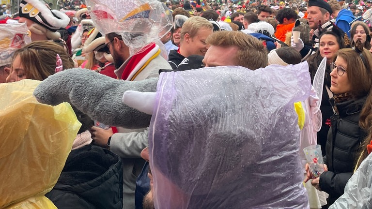 Viele Menschen feiern Fastnachtsauftakt auf dem Schillerplatz - viele in Regenkluft.