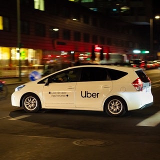 Ein Auto des Diensteleisters Uber fährt über eine Kreuzung im Dunklen. Die Uber-Fahrerinnen und -Fahrer waren in Wiesbadne zuletzt in Kritik geraten, weil sie sich nicht an Regeln halten sollen.