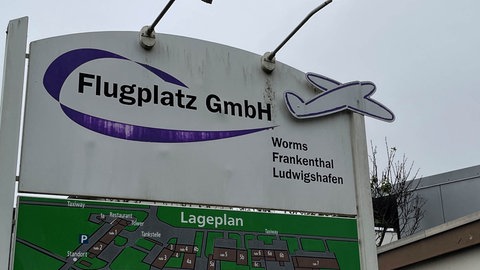 Ein Schild auf dem Flugplatz Worms mit der Aufschrift "Flugplatz GmbH", an dem der Regen die Farbe weg gewaschen hat.