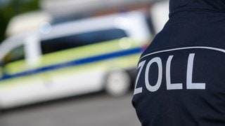 Ein Zoll-Mitarbeiter vor einem Polizeiwagen. In Worms ist dem Zoll nach eigenen Angaben ein Schlag gegen ein Schwarzarbeiter-Ring gelungen. 